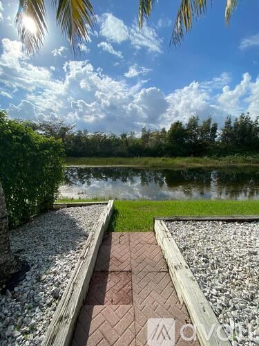 A serene landscape with a pond, trees, and a clear sky.