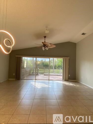 A room with a ceiling fan and sliding glass doors leading to a backyard.