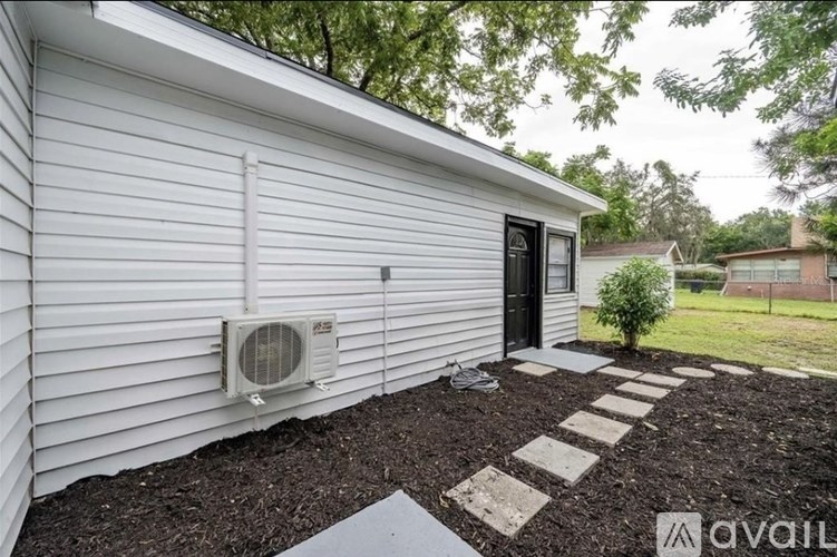 A small white house with a black door and a window, and a small tree in front of it.