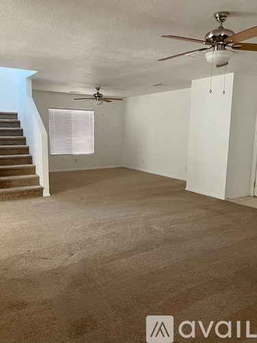 A room with a carpeted floor, a staircase, and two ceiling fans.