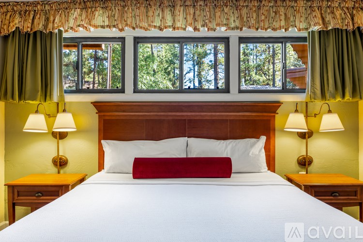 A bed with a red pillow in the middle is in front of a window with green curtains.