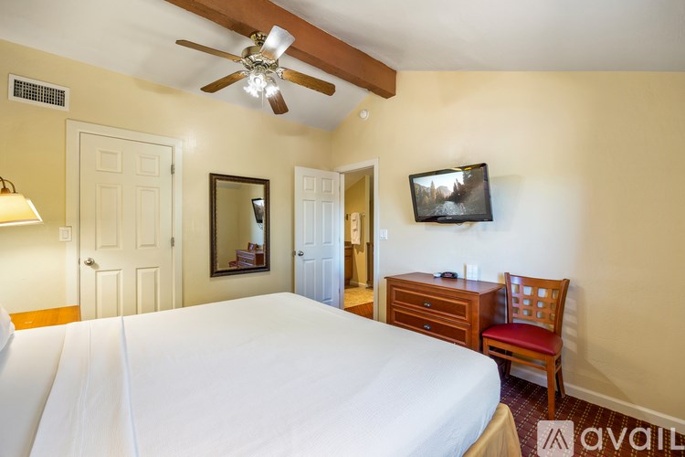 A bedroom with a large bed, a ceiling fan, a chair, and a television.