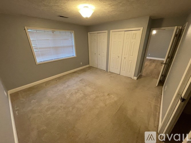 A room with a carpeted floor, a window with blinds, and a door.