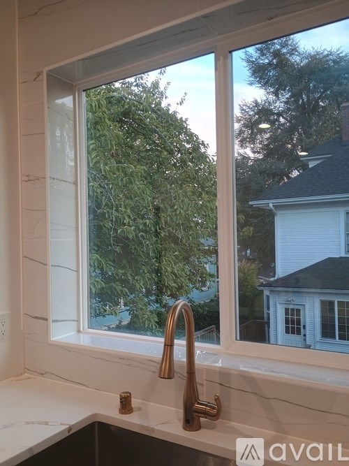 A kitchen window with a view of a house and trees outside.