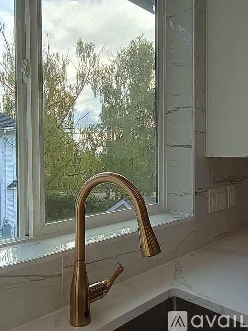 A kitchen sink with a gold faucet and a window in the background.