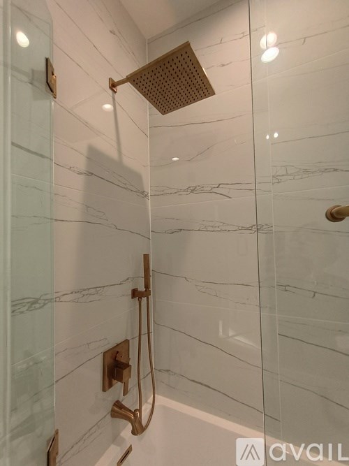 A shower area with a glass door and a marble wall.