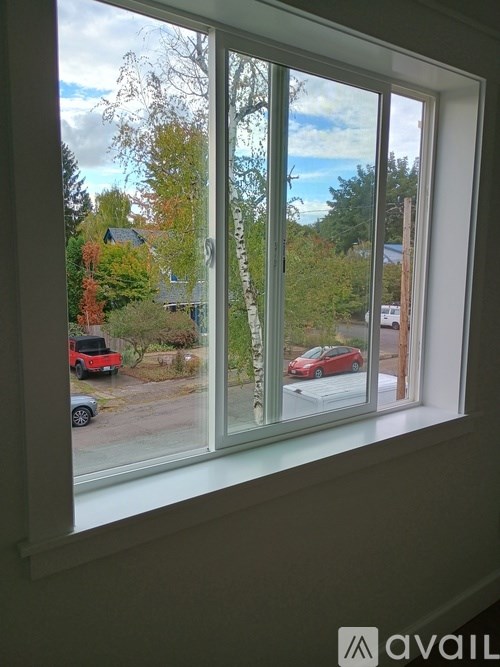 A window with a view of a red car and trees outside.