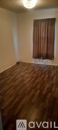 A room with wooden flooring and a window with brown curtains.