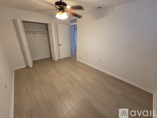 A room with a ceiling fan and light, wooden flooring, and a closet with a door and a shelf.