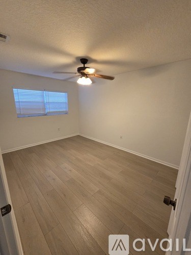 A room with a ceiling fan and light, wooden flooring, and a window with blinds.