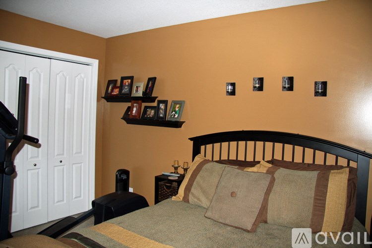 A bedroom with a bed, a white door, and a shelf with picture frames on it.
