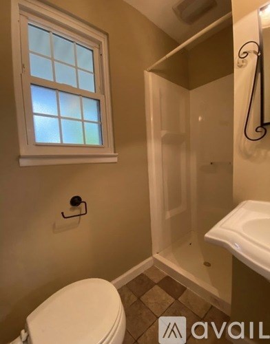 A bathroom with a toilet, a window, and a shower.