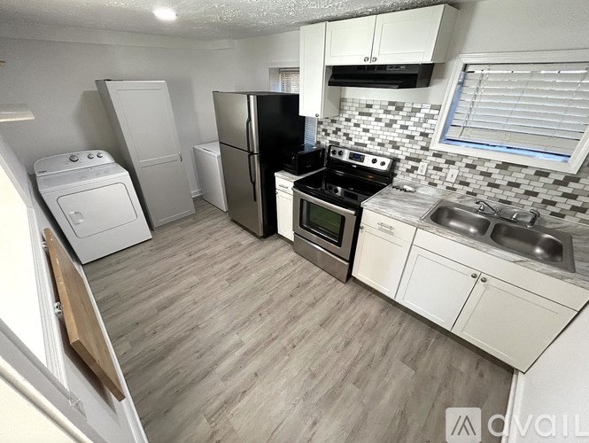 A kitchen with a black refrigerator, white cabinets, and a wooden floor.