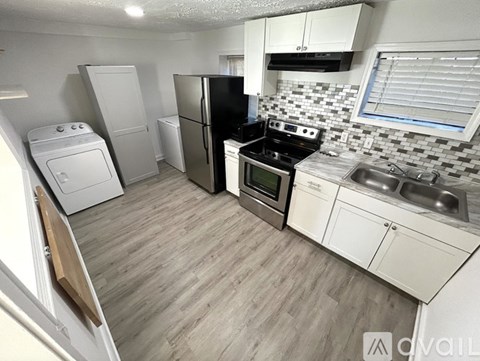 A kitchen with a black refrigerator, white cabinets, and a wooden floor.