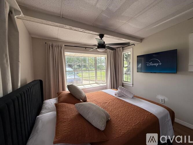 A bedroom with a bed, pillows, a ceiling fan, and a Disney logo on the wall.