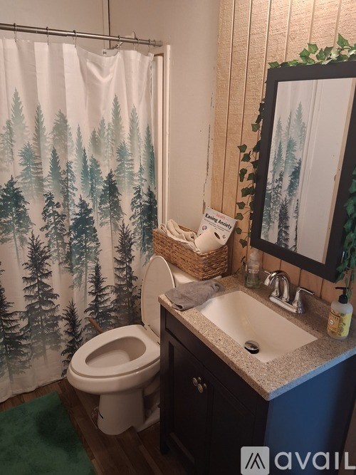 A bathroom with a toilet, sink, and a shower curtain with a forest pattern.