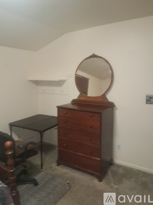 A wooden dresser with a round mirror on top sits in a room with a desk and chair.