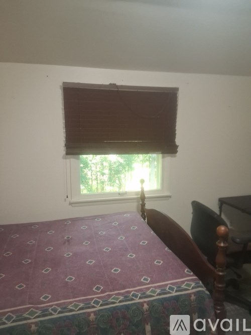 A bedroom with a bed and a window with blinds.