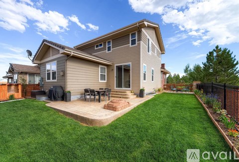 A house with a brown roof and a beige exterior is surrounded by a green lawn and a wooden deck.