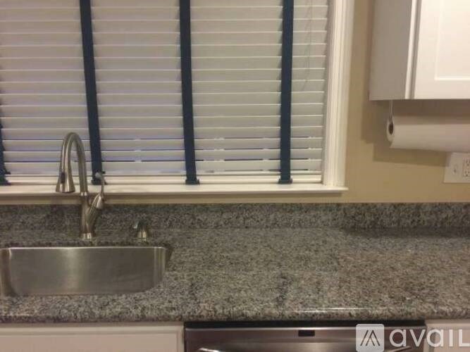 A kitchen sink under a window with blinds.