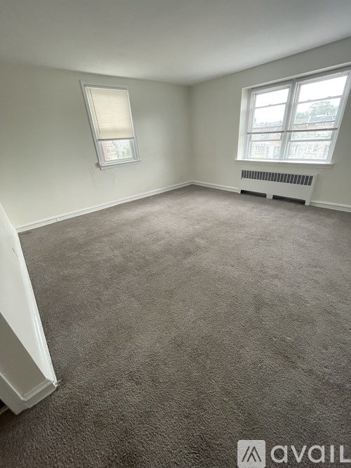A carpeted room with a window and a radiator.