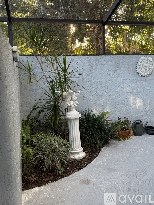 A white pillar in a garden with a wall and plants.