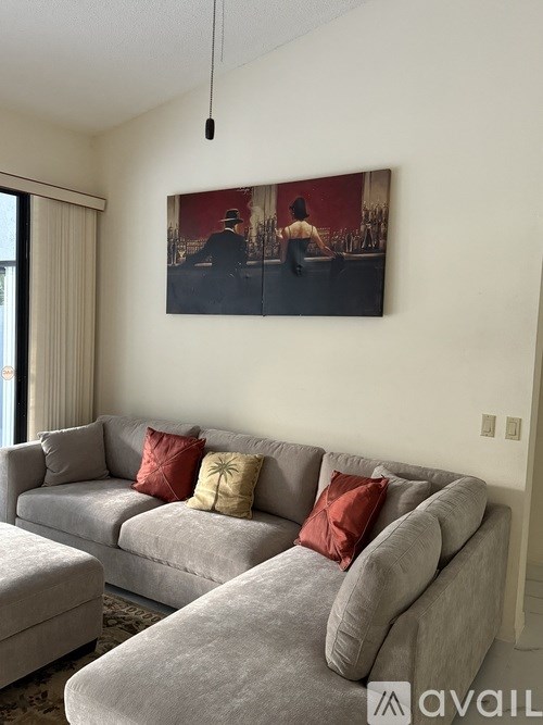 A living room with a grey couch and a painting on the wall.