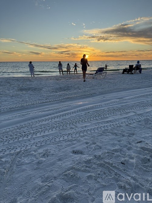 A group of people are walking on the beach at sunset.