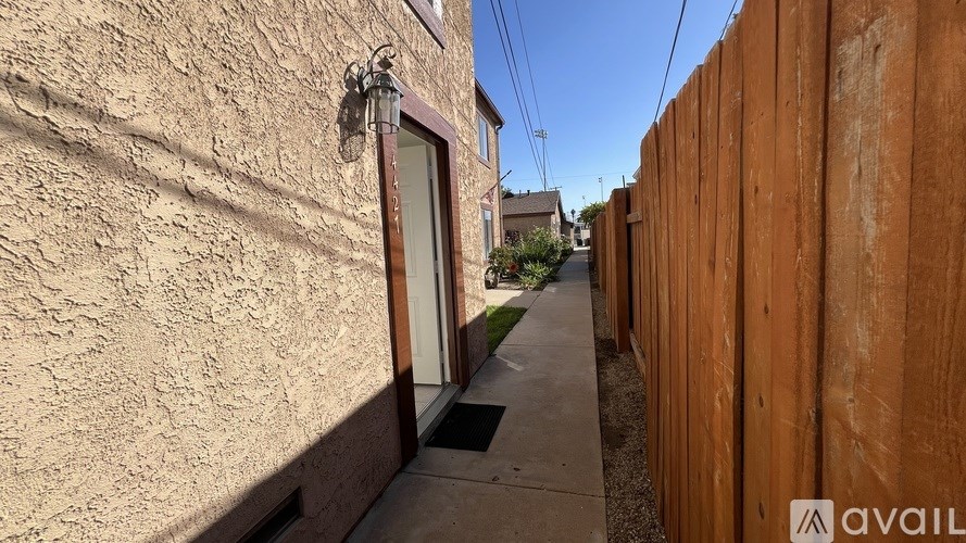 A narrow alley with a wooden fence on one side and a building with a window and a lamp on the other.