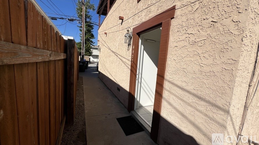 A narrow alley with a wooden fence on the left and a building with a window and a door on the right.