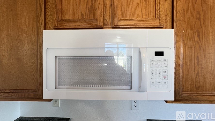 A white microwave oven with a digital display and control panel is mounted on a wooden cabinet.