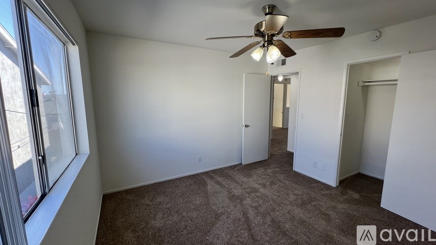 A room with a carpeted floor, a ceiling fan, and a window with a view of a building outside.