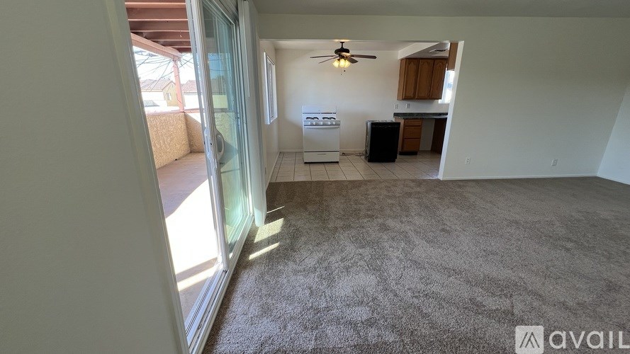 A carpeted room with a ceiling fan and a kitchen area in the background.
