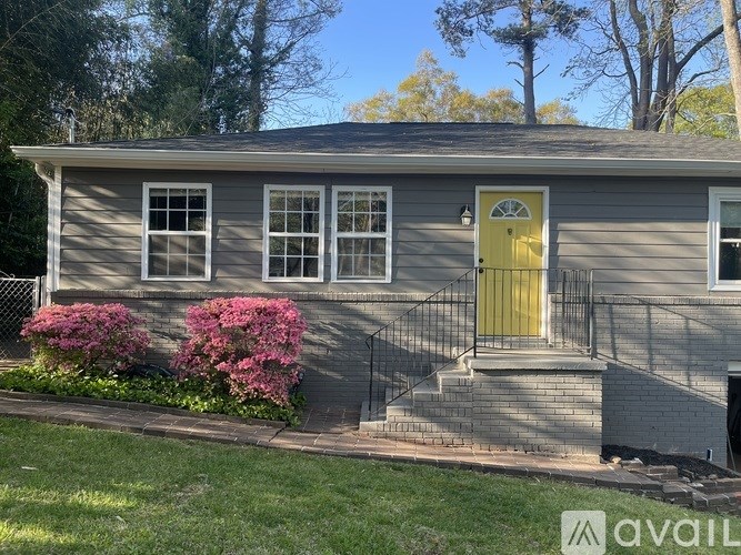 A house with a yellow door and a small front yard with pink flowers.