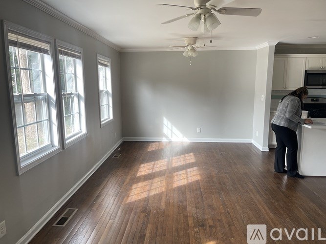 A woman is standing in a room with wooden floors and a ceiling fan.
