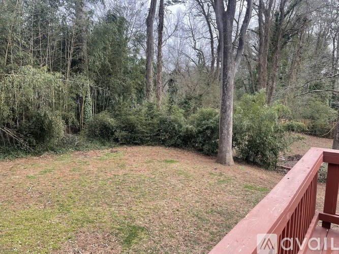 A backyard with a wooden deck and a grassy area surrounded by trees.