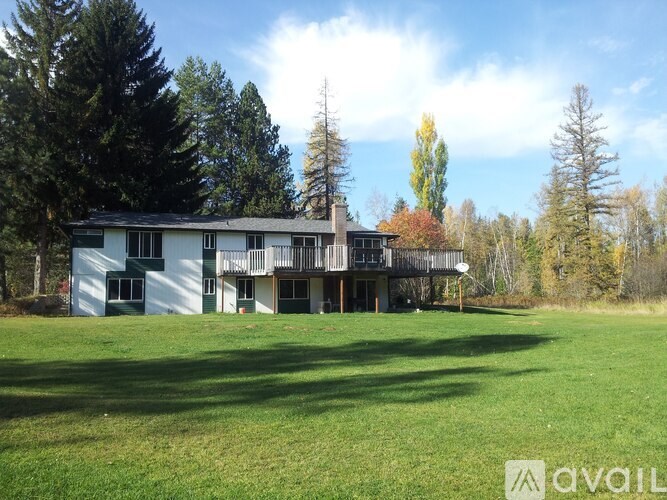 A large white house with a balcony is surrounded by trees.