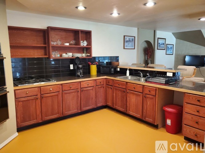 A kitchen with wooden cabinets and a red trash bin.