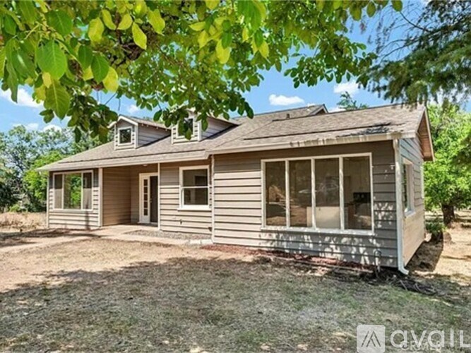 A house with a brown roof and grey siding is surrounded by trees.