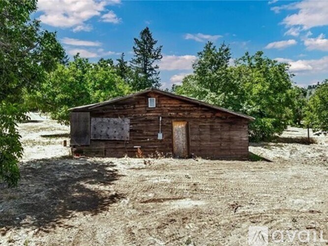A small wooden cabin sits in a field with trees in the background.