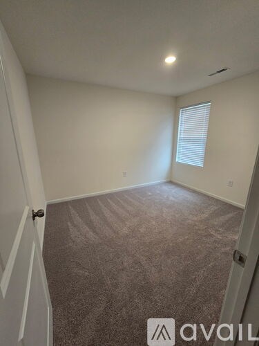A room with carpeted floor and a window with blinds.