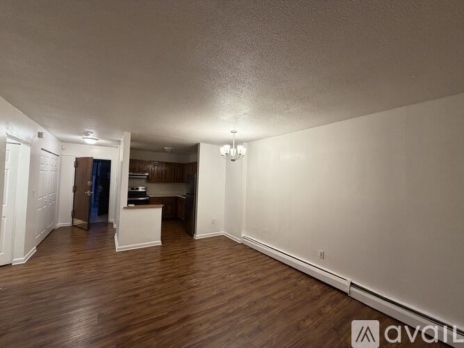 A spacious room with wooden floors and white walls, currently empty and available for rent.