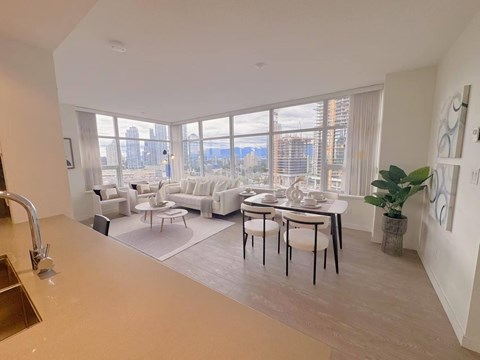 A modern kitchen with a dining table and chairs in the foreground and a living room with a couch and chairs in the background.