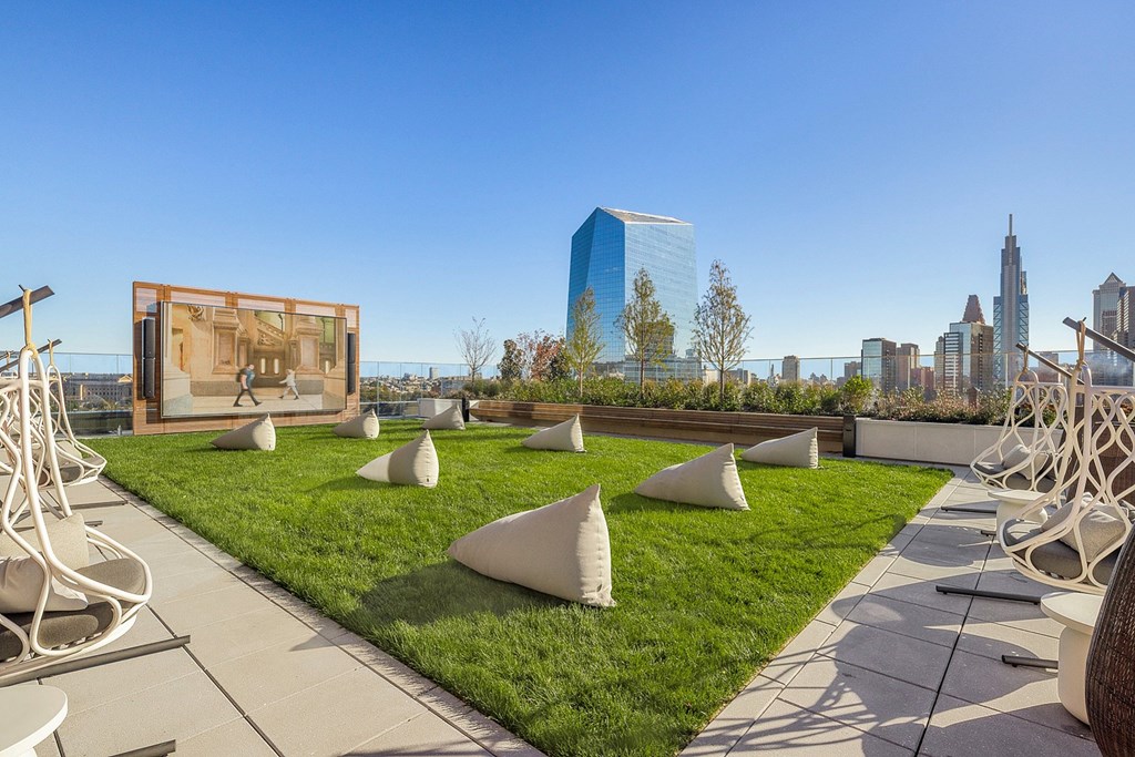 A modern outdoor seating area with white chairs and a large screen in the background.