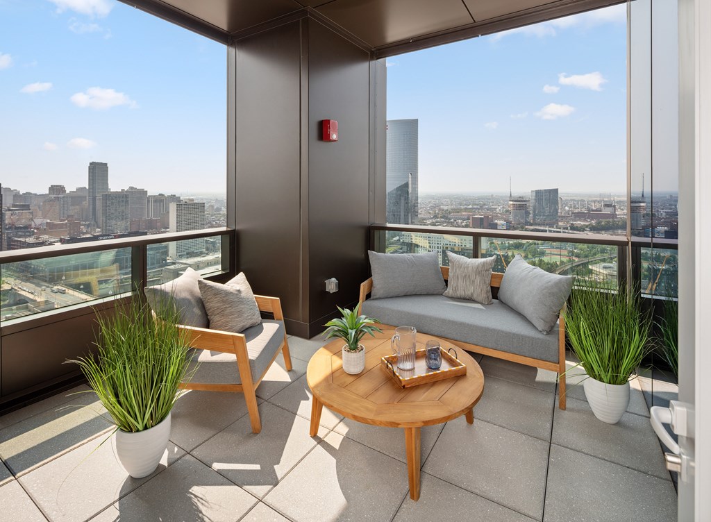 A balcony with a table, two chairs and a couch with a city view in the background.