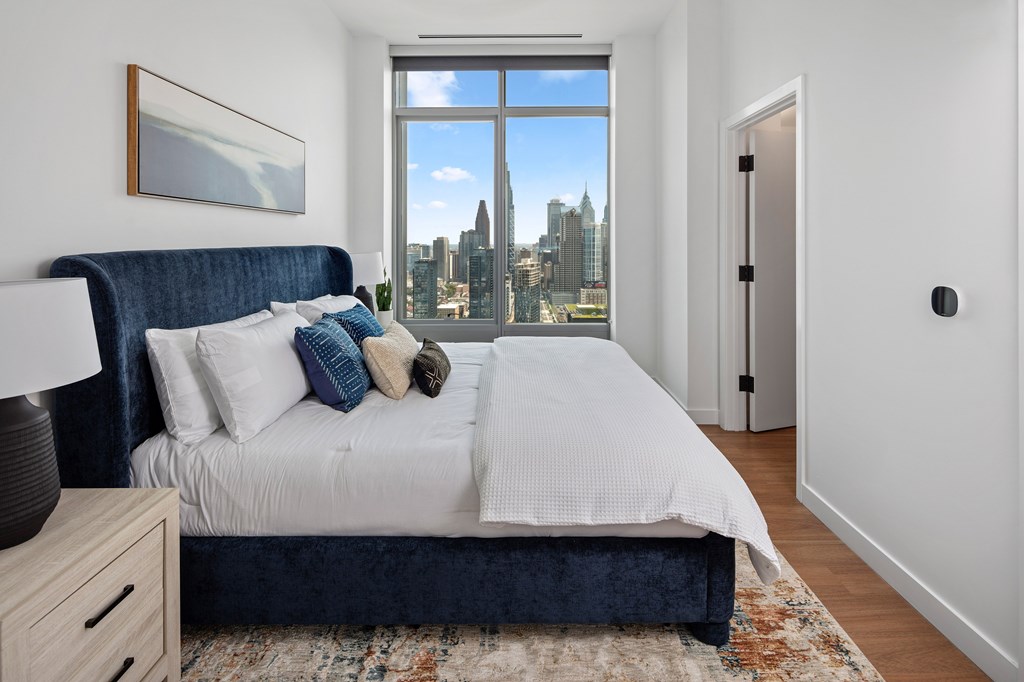 A bedroom with a large bed and a city view through the window.