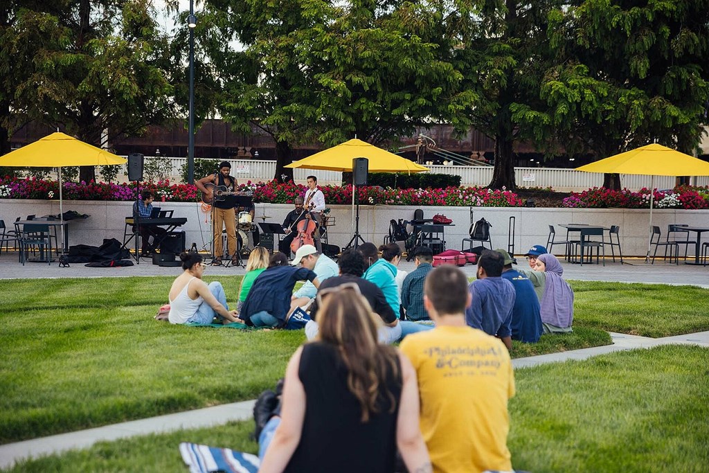A group of people are sitting on the grass and watching a performance on a stage.
