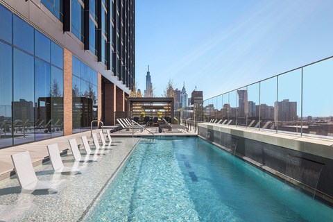 A long row of white chairs are lined up on a balcony overlooking a blue pool.