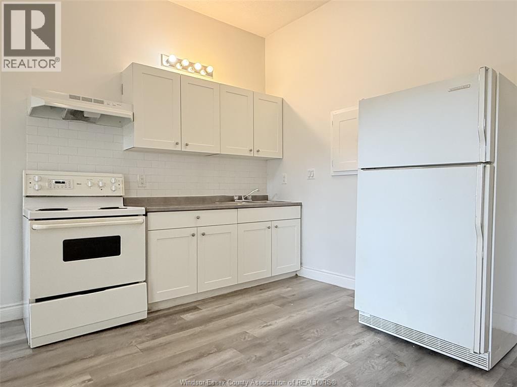 A white fridge stands in a kitchen with white appliances and cabinets.