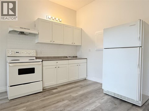 A white fridge stands in a kitchen with white appliances and cabinets.